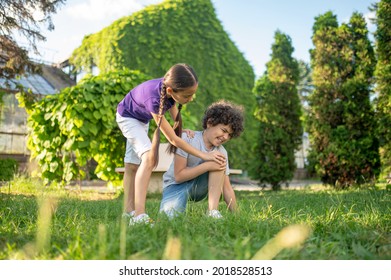 Girl Bending Over To Boy Sitting On Grass