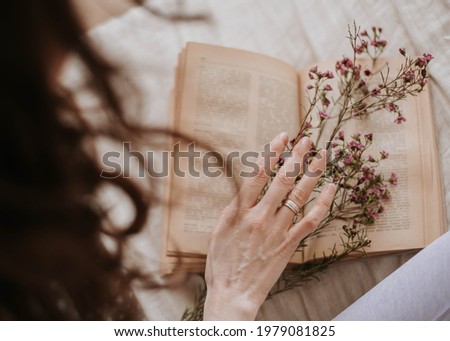 girl bent over a vintage book: thin hand, old pages and summer flowers