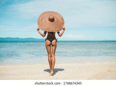 Girl In A Big Hat Stands With His Back On The Beach