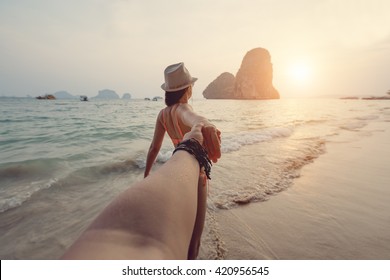 Girl in a bikini holding a guy's hand on the beach