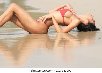 The girl in a bikini on the beach, there is a red shadow reflected on the water.