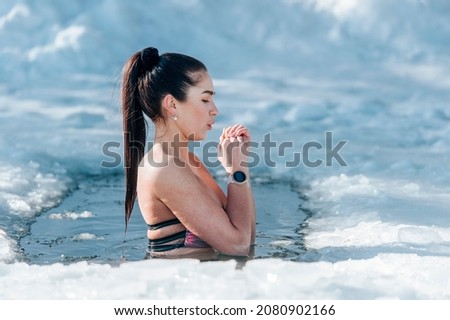 Girl with bikini and a watch in frozen lake ice hole. Woman hardening the body in cold water. Good immunity is protection against many diseases. Vintage color filter