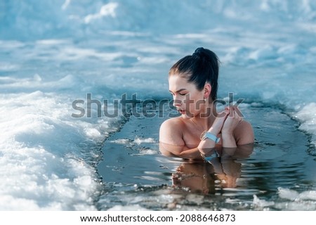 Girl with bikini and a watch in frozen lake ice hole. Woman hardening the body in cold water. Good immunity is protection against many diseases. Vintage color filter
