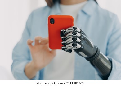 Girl with bionic prosthetic arm, holding smartphone in hands. Close up female with disability adjusting gesture and grasp of high tech robotic artificial limb.