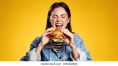 La chica muerde con placer la hamburguesa de queso. Mujer comiendo hambuger, pedir hamburguesa para llevar comida en el restaurante de comida rápida