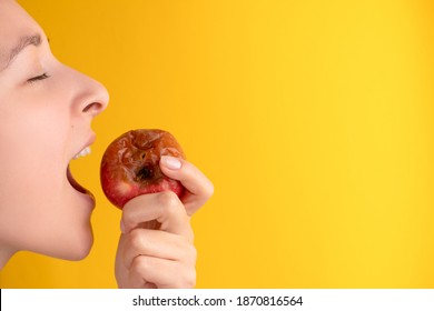 The Girl Bites A Rotten Apple With A Worm On A Yellow Background. Expired Products, Junk Food.