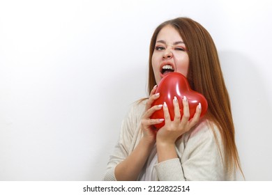 Girl bites a toy heart. Attractive young woman biting a red heart shaped balloon. Funny Valentines Day. Woman winks, teeth bared, shows passion