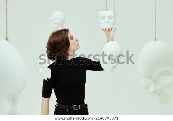 A girl in black clothes
tries on different masks-roles, standing surrounded by different
masks in a white room. Human roles. Hypocrisy. Mental
disorders.
