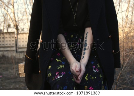 the girl in the black coat with the accessory in the form of the Eiffel tower in a skirt with flowers  with tattoo with the phases of the moon on the hand