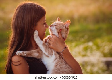 Girl in black dress holds a red cat standing on the field