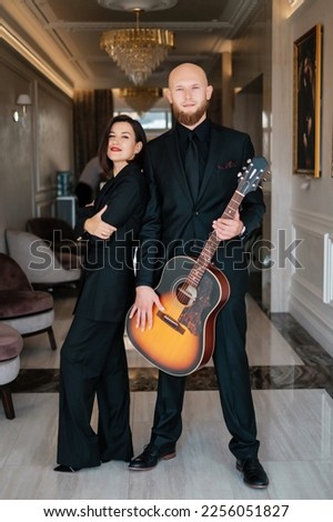 A girl in a black dress and musician. Lovely duet posing with guitar.
