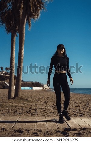 a girl in black sportswear returns from training. athletic girl after training on the beach.