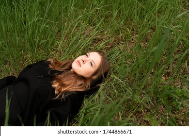 a girl in a black sweatshirt lies in a meadow of fresh grass enjoys calm, view from the top