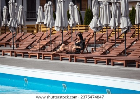 A girl in a black swimsuit rests on a sun lounger by the pool.
