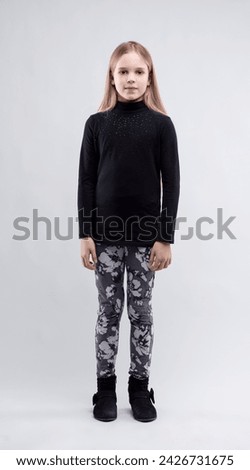Girl in a black top and patterned leggings stands with a subtle confidence against a neutral backdrop