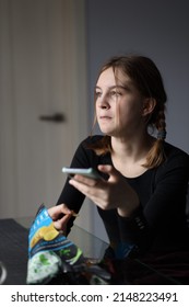 Girl In Black T-shirt Sits In Kitchen Holding Phone In Her Hand And Eating Chips