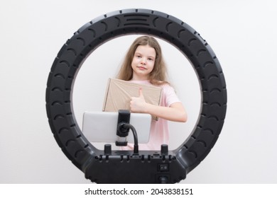 a girl blogger, in the center of a circular lamp and a smartphone, makes an overview of the package for unpacking and shows the class - Shutterstock ID 2043838151