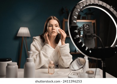 Girl blogger recording video on smartphone camera how to care for skin, uses cosmetic product at home. Copy space - Powered by Shutterstock