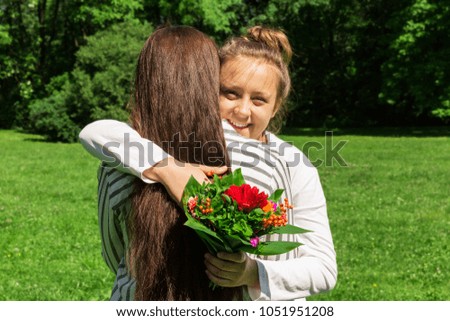 A girl with blond hair combed in a bun, gives her mother a bouquet of red flowers for Mother's day. 26th of May.