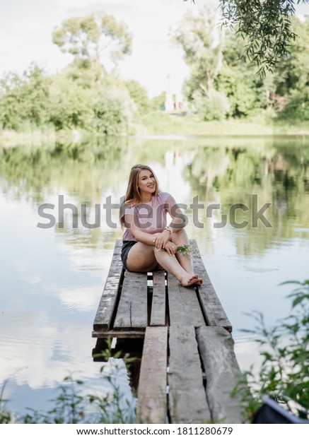 Girl with\
blond hair from Eastern Europe, is laughing and sitting on the\
pier, holding chamomile . High quality\
photo