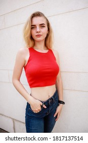 Girl with blonde hair in a red top and blue jeans. Shooting on steet.Teenager. Stylish clothes