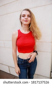 Girl with blonde hair in a red top and blue jeans. Shooting on steet.Teenager. Stylish clothes