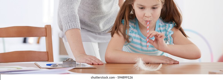 Girl blowing in the feather through straw as mouth system exercise