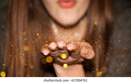 A girl blowing millions of pieces of gold glitter from her hand