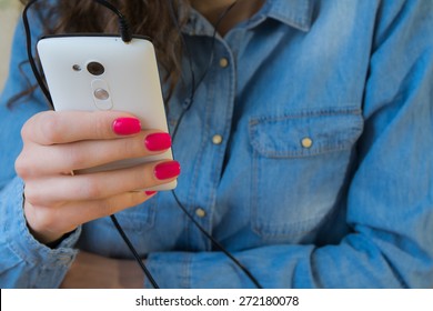 The Girl In Blue Denim Shirt With Red Nail Polish Listens To Music On A White Phone.