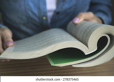 The Girl In The Blue Denim Shirt Sitting At The Table Reading A Paperback Book. Vintage Photo. Closeup.