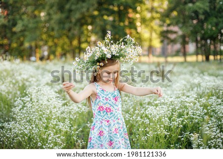 a girl in a blue dress with flowers stands in a chamomile field