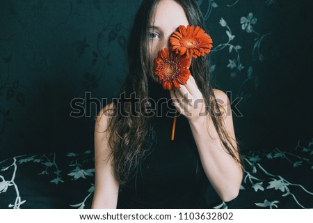 a girl with blue eyes and long hair covering herself with a gerbera flower