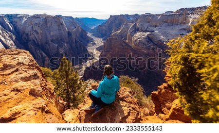 Girl in a blue jacket sits on rocks and admires the unique canyon from Observation Point (East Mesa Trail) in Zion National Park, Utah, USA. Winter in Utah	