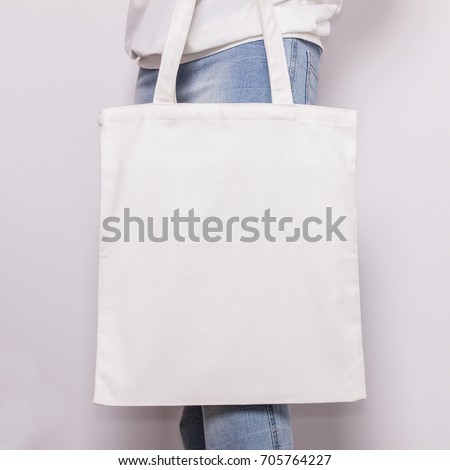 Girl in blue jeans holds blank cotton eco tote bag, design mockup.