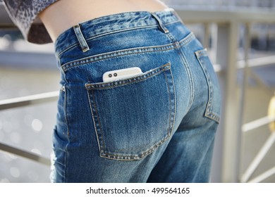 Girl in blue jeans with modern dual camera smart phone in back pocket. Focus on double lens camera module. 