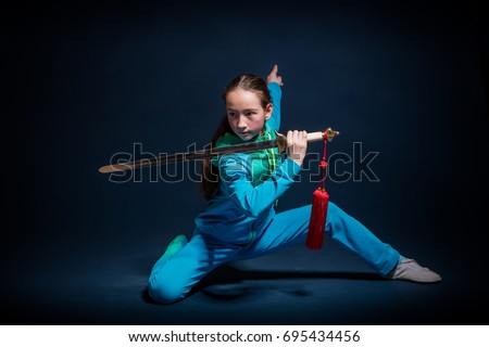 Girl in a blue wear engaged wushu against a dark background