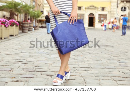 Girl in blue and white leather sandals, striped dress and big blue leather handbag in hand. Woman in summer street look walking around the city on sunny summer day.