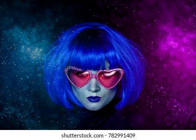 Girl in blue wig and pink glasses. The mystical picture. Alien with blue skin. In the glare