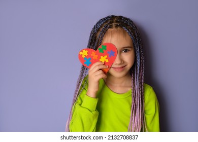 A Girl With Blue-purple Afro Pigtails In A Light Green Top Holds A Heart With Puzzle Pieces In Her Hands As A Sign Of Solidarity With People Suffering From Autism Spectrum Disorder. World Autism Day