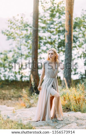 Girl in a boudoir dress in a pine forest. Standing on the rocks in a thin flying dress. Unity with nature at the wedding. Bride at sunset