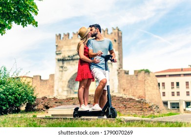 Girl And Boy Kiss In A Romantic Moment On A Eco-scooter In Front Of An Arch - Concept About Eco Travel And Respecting The Nature