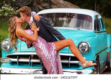 Girl And Boy Kissing While Posing For High School Senior Prom Photos With Old Blue Car With White Hood No Logos