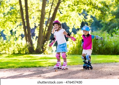 Girl and boy learn to roller skate in summer park. Children wearing protection pads and safety helmet for safe roller skating ride. Active outdoor sport for kids. Siblings help and support each other