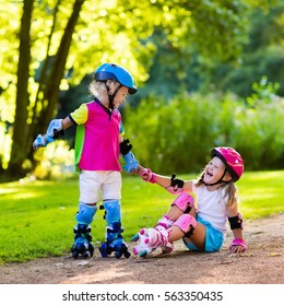 Girl and boy learn to roller skate in summer park. Children wearing protection pads and safety helmet for safe roller skating ride. Active outdoor sport for kids. Siblings help and support each other.