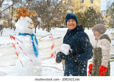 A Girl And Boy Play With Snow On A City Street And Make A Snowman