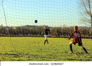 Girl And Boy Playing English Football On A Countryside Sports Field. UK