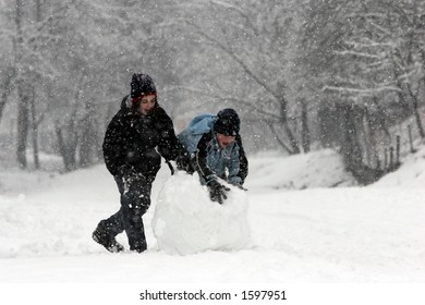 Girl And Boy Rolling A Huge Snowball