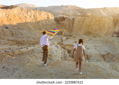 A girl and a boy are running around a sandy quarry with a bright kite. - Shutterstock ID 2233887615