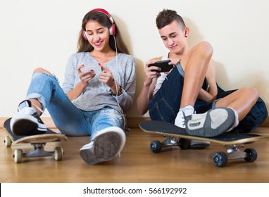 Girl and boy teens playing games online on smarthphones in living  room - Powered by Shutterstock