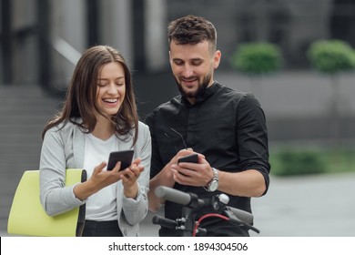 Girl and boy using smartphones to rent an e-kick vehicle. Couple with mobile phones using eco transport. Electric scooter  in urban background. 